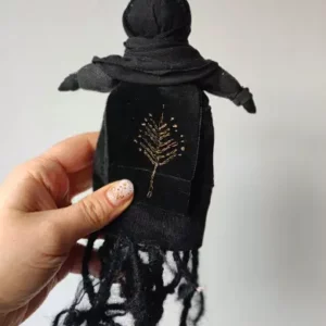 Czarna Lalka wykonana ręcznie z tkanin i sznurka. Ma czarne ciało, czarną twarz i czarne korzenie zamiast nóg. Jest wielkości trochę większej od dłoni.