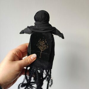 Czarna Lalka wykonana ręcznie z tkanin i sznurka. Ma czarne ciało, czarną twarz i czarne korzenie zamiast nóg. Jest wielkości trochę większej od dłoni.