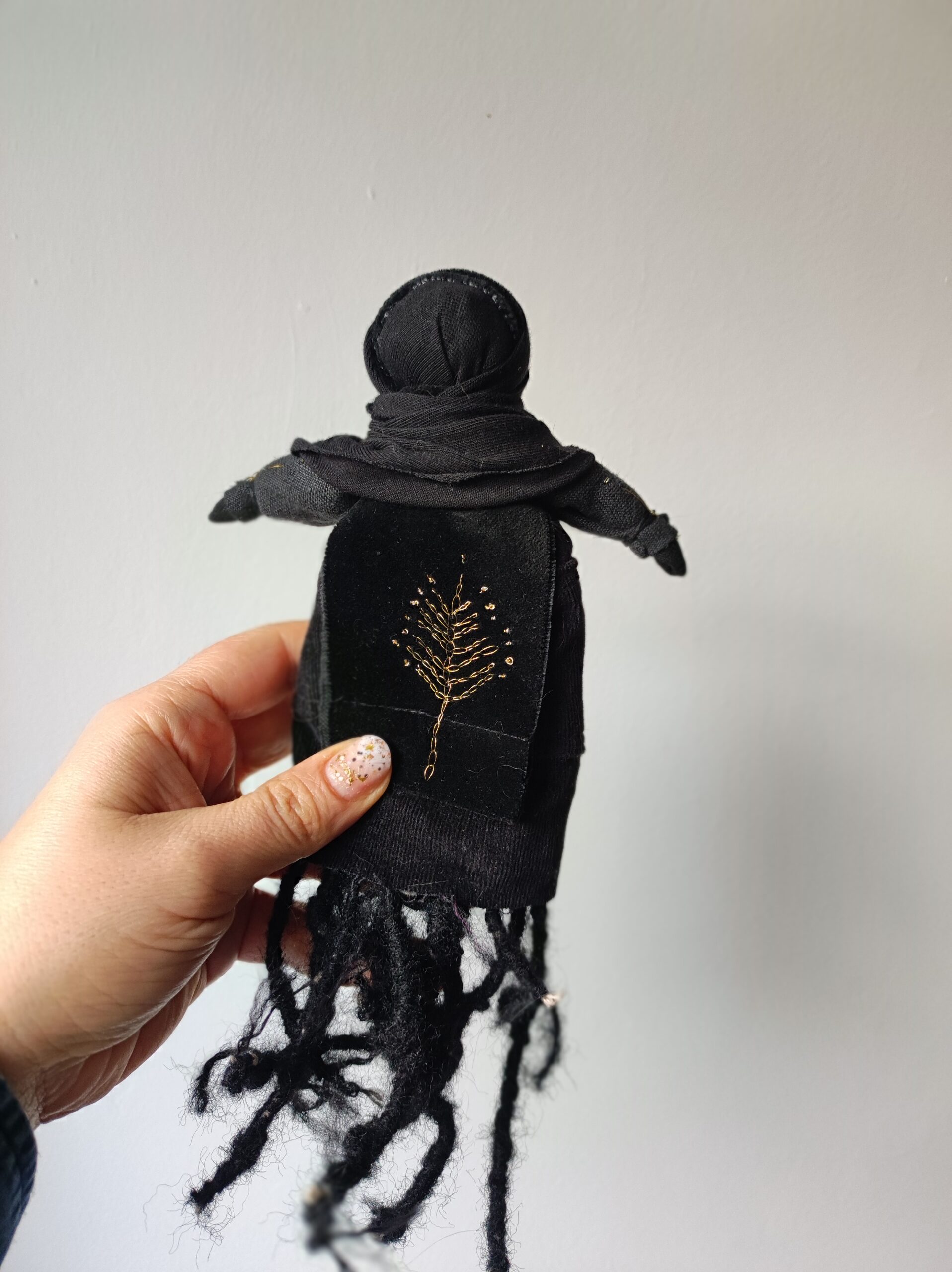 Czarna Lalka wykonana ręcznie z tkanin i sznurka. Ma czarne ciało, czarną twarz i czarne korzenie zamiast nóg. Jest wielkości trochę większej od dłoni.