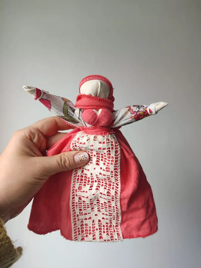 Motanka, tradycyjna lalka mocy, w kolorach brzoskwiniowych, z koronkowym fartuszkiem.