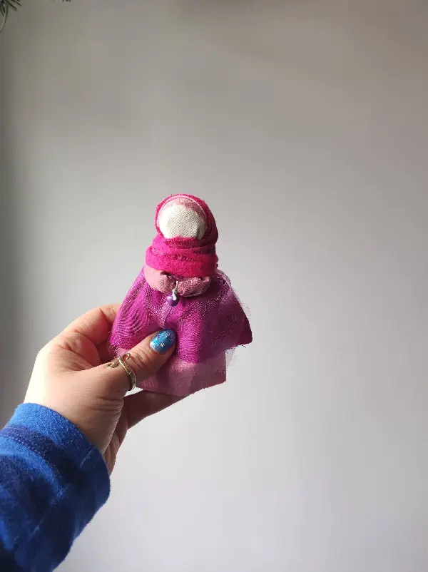 Lalka motanka wykonana z kawałków tkanin i nici. Motanka ma na sobie ubranie w kolorze różowym