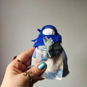 Lalka Mocy zamotana z naturalnych tkanin i nici ze wzorem bławatka na fartuszku.