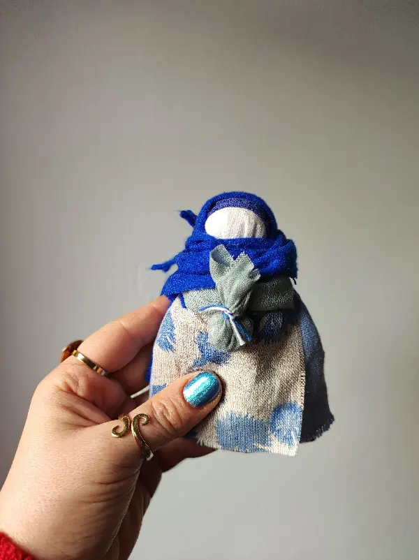 Lalka Mocy zamotana z naturalnych tkanin i nici ze wzorem bławatka na fartuszku.